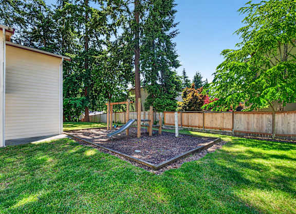 Shared community playground near building, surrounded by pine trees and grass.
