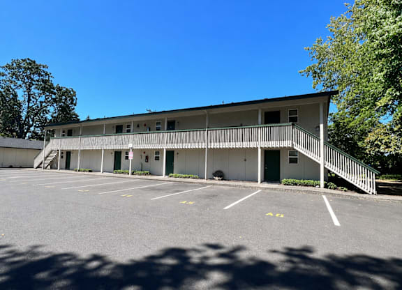 A white building with a green door and a parking lot in front.