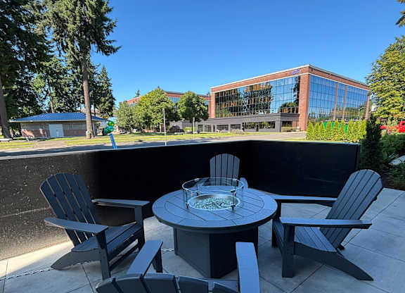 A chair and table are in the foreground with a building and trees in the background.