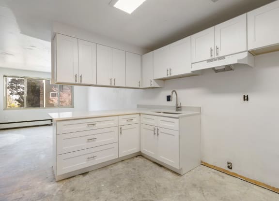 an empty kitchen with white cabinets and a sink and a window