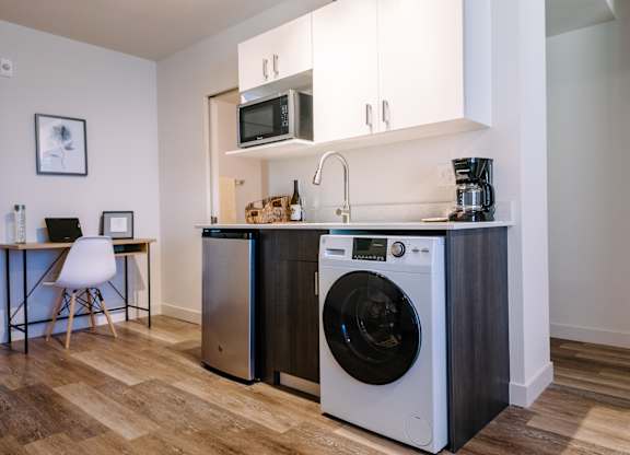 A Bode125 studio kitchen with a washer and dryer., refrigerator, microwave, and desk off to the left