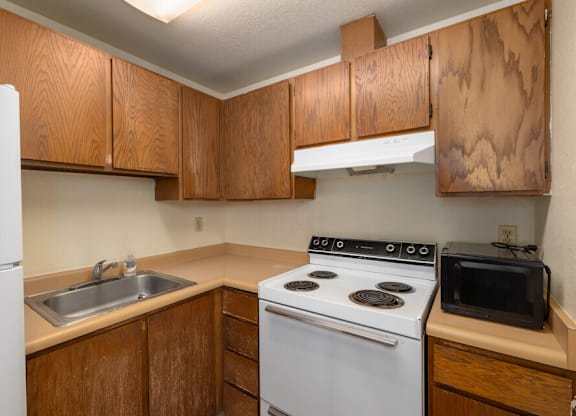 A kitchen with a white fridge, white stove, and brown cabinets.