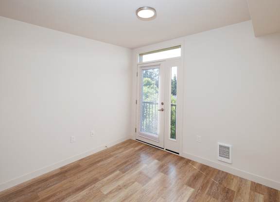 A room with a wooden floor and a door leading outside.