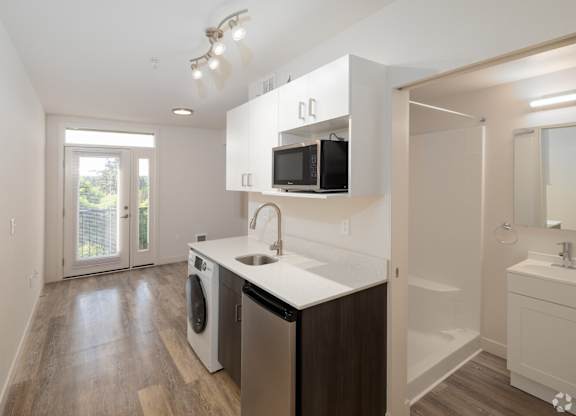 Modern kitchen with stainless steel appliances, white finishes, and open-concept living in our MFTE studio apartment homes