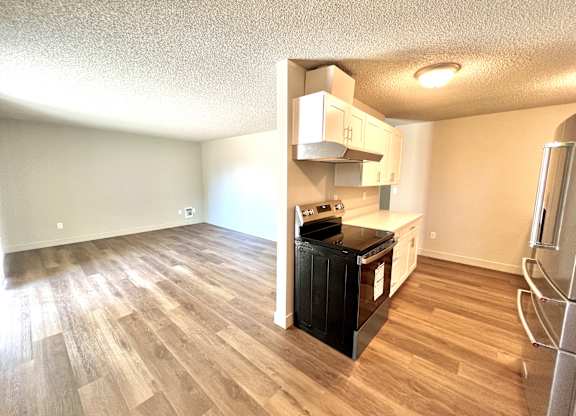 2-bedroom apartment kitchen and living room with a black stove, vinyl plank floors., and white cabinets