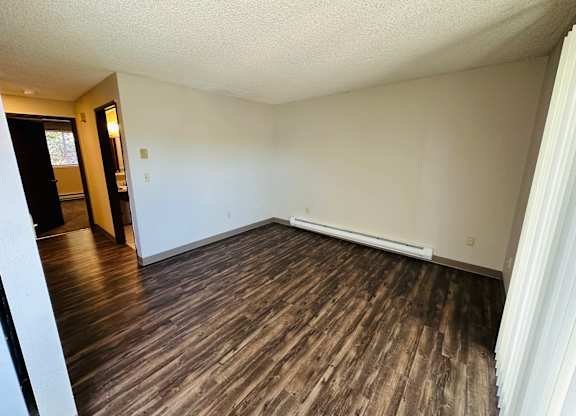 1-bedroom Living room with wood-look vinyl plank flooring, neutral walls, and open layout near hallway and bathroom.