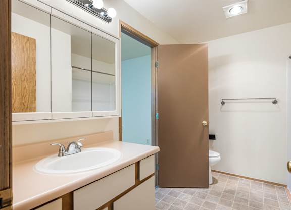 A bathroom with a sink, mirror, toilet and a brown door.