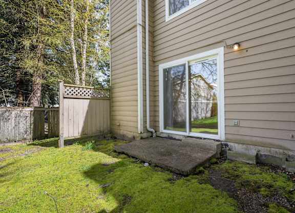 A backyard with a moss-covered lawn and a small concrete patio.