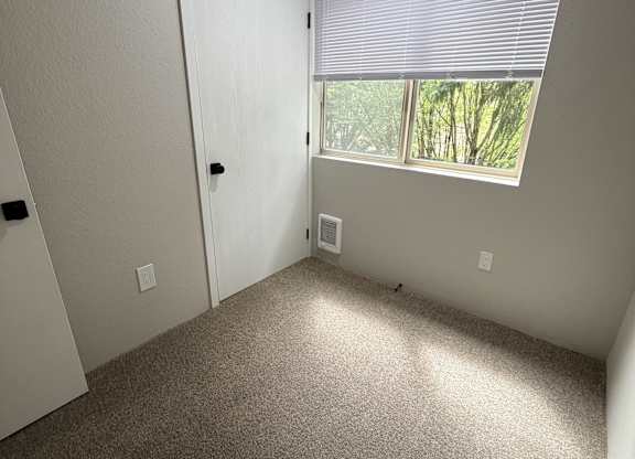A room with a carpeted floor, a door, and a window with blinds.