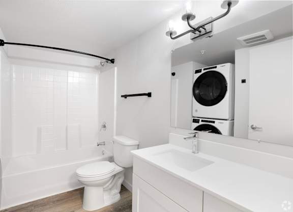 A white bathroom with a toilet, sink, and a washing machine in the corner.