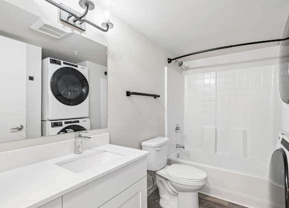 A white bathroom with a toilet, sink, and washer and dryer.