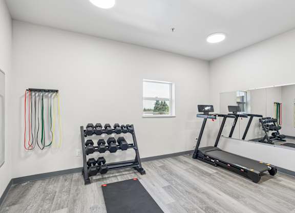 A well-lit home gym with a treadmill, dumbbells, and resistance bands.