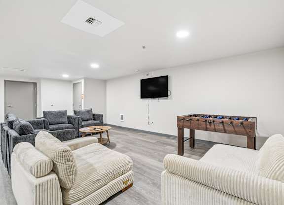 A living room with a white couch, grey couch, and a wooden table with a TV mounted on the wall.