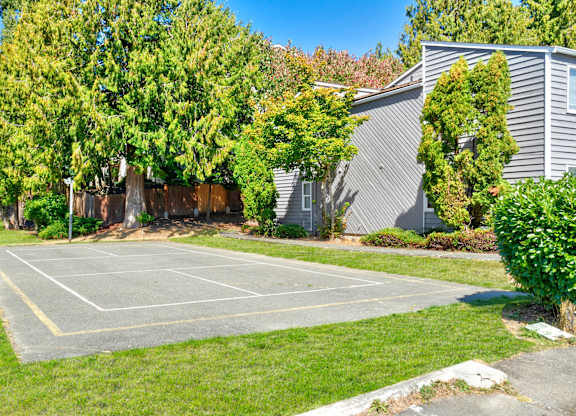 A tennis court surrounded by green grass and trees.