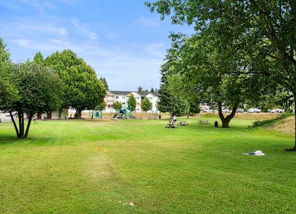 A park with a grassy field, trees, and picnic tables.