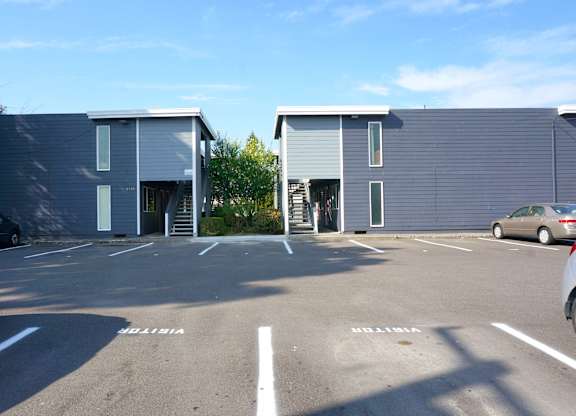A parking lot with two buildings and cars parked in front.