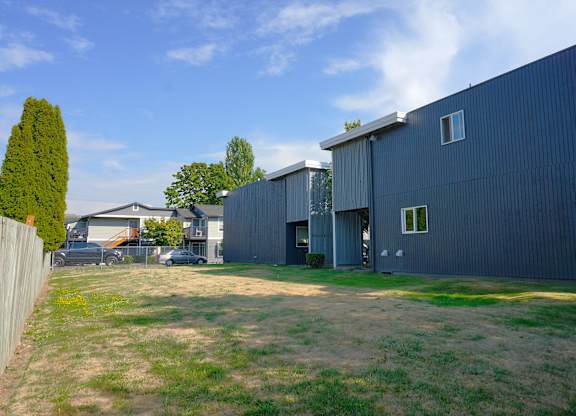 A large grey building with a small white window sits in a grassy lot.