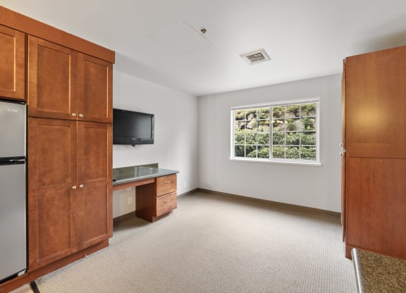 a room with a desk and a refrigerator and a window