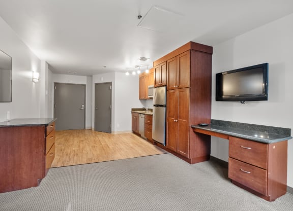 the living room and kitchen of an apartment with wood cabinets and a tv