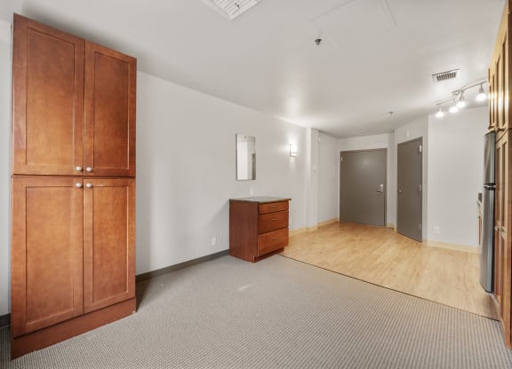 a living room with white walls and wooden furniture and a refrigerator