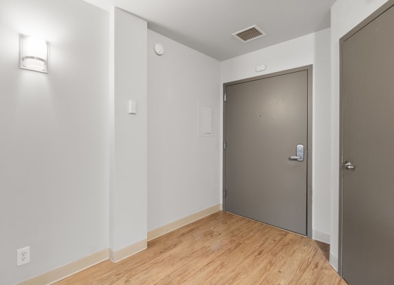 the living room of an apartment with a wood floor and a grey door