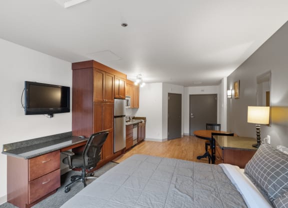 a bedroom with a bed and a desk and a kitchen with a tv