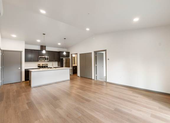 A spacious room with wooden flooring and a kitchen area in the background.