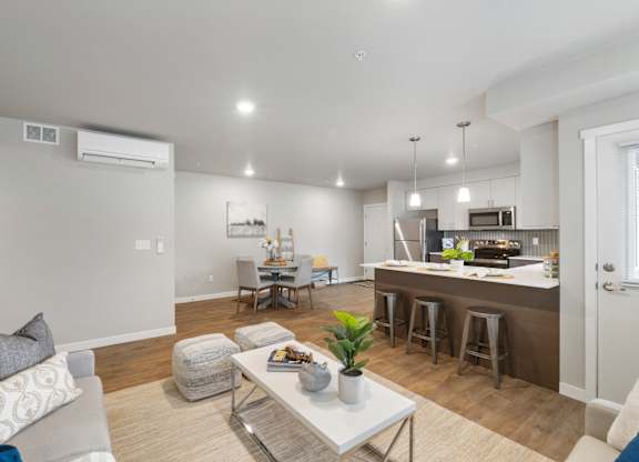 A modern living room with a grey couch, a white coffee table, and a kitchen area in the background.