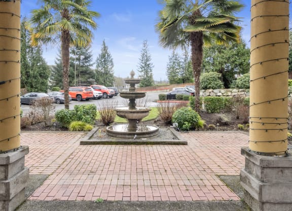 a fountain in a courtyard with palm trees and a parking lot