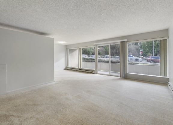 the living room and dining room of an apartment with large windows and carpeting