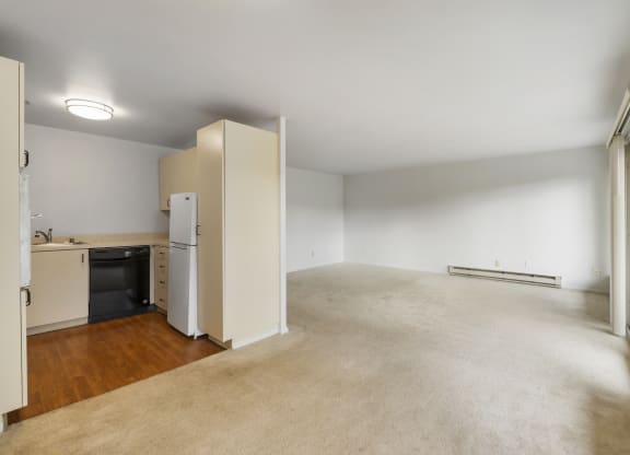 the living room and kitchen of an apartment with white walls and wood flooring