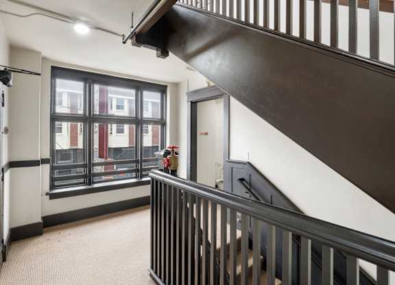 A black metal staircase with a white wall and a window with a view of a building.