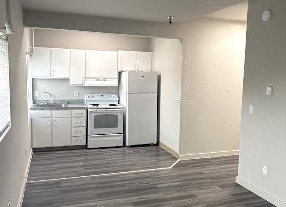 A kitchen with white appliances and cabinets is visible from a hallway.