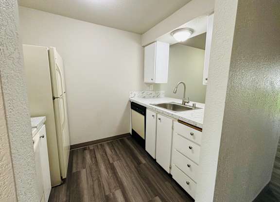 A small white kitchen with wood floors and a white refrigerator.