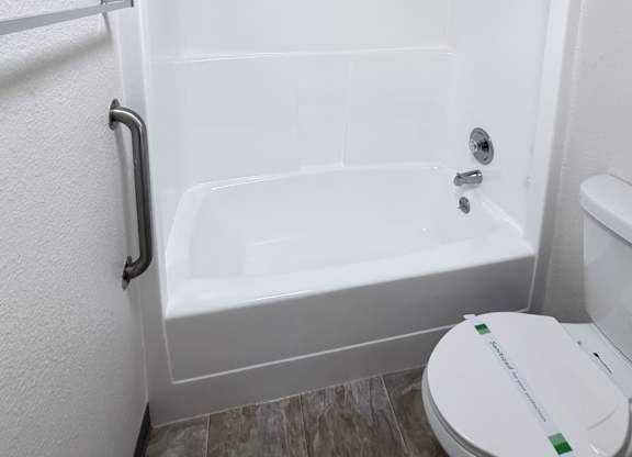 A white toilet with a green stripe is in a bathroom with a white tub.