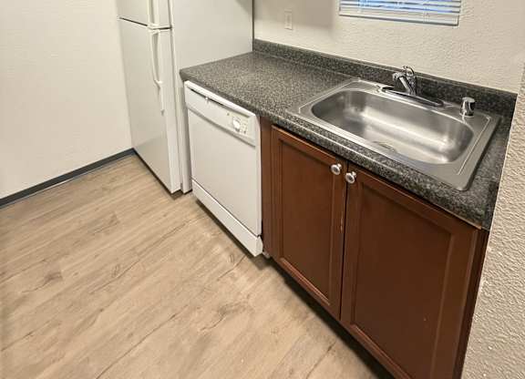 A kitchen with a white refrigerator, brown cabinets, and a granite countertop.