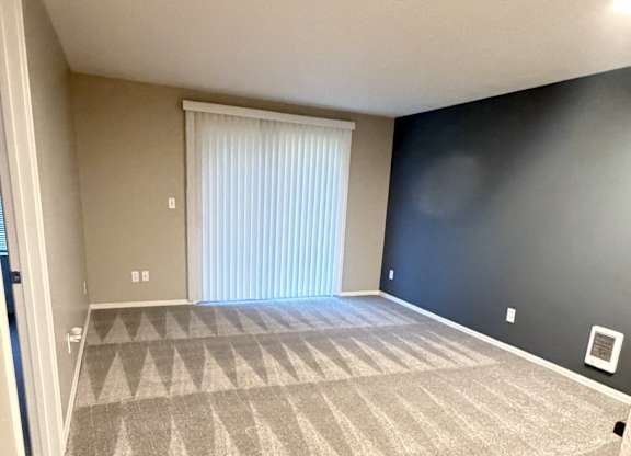 A room with a carpeted floor and a window with blinds.