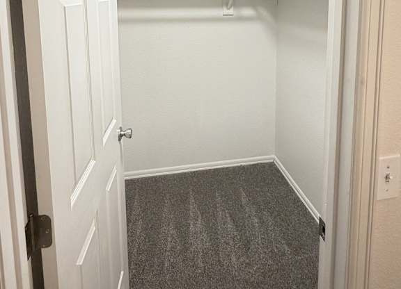 A white door is open to a small, empty room with a grey carpet.