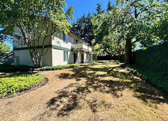 A white house with a green lawn and trees in front.