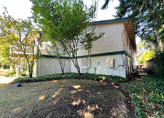 A white building with a green trim is surrounded by trees and shrubs.