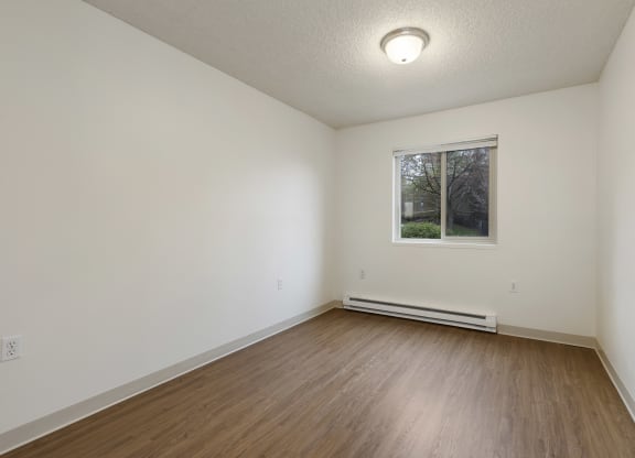 a bedroom with white walls and wood floors and a window