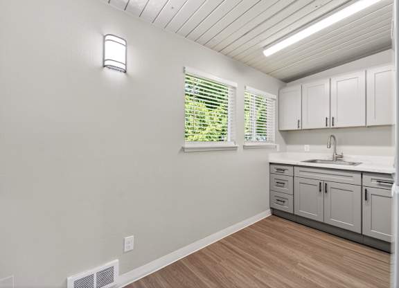A kitchen with white cabinets and a window with blinds.