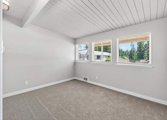 A room with a carpeted floor and a window showing a view of trees and a house.