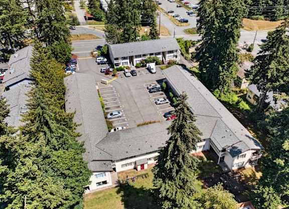 A parking lot is surrounded by trees and a building.