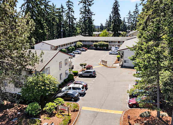 A parking lot is surrounded by trees and a white building.