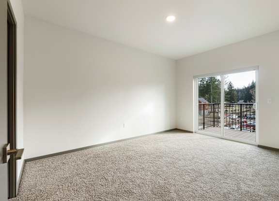 A room with a carpeted floor and a sliding glass door leading to a parking lot.