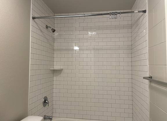 A white tiled shower with a white toilet and a white shower head.