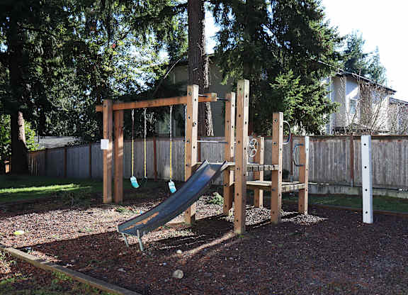 A wooden playground with a green slide and swings at Horizon Park Apartments in Edmonds, WA