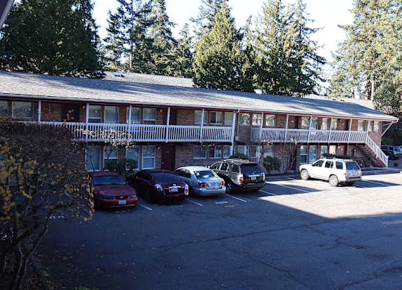 JHorizon Park Apartments parking lot with cars and a building in the background, surrounded by pine trees