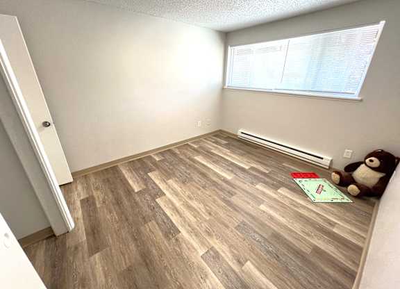 A room with wooden flooring and a teddy bear on the floor.